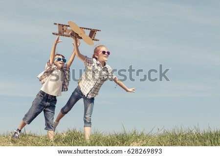 Two little kids playing with cardboard toy airplane in the park at the day time. Concept of happy game. Child having fun outdoors. Picture made on the background of blue sky.