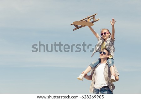 Father and daughter playing with cardboard toy airplane in the park at the day time. Concept of friendly family. People having fun outdoors. Picture made on the background of blue sky.