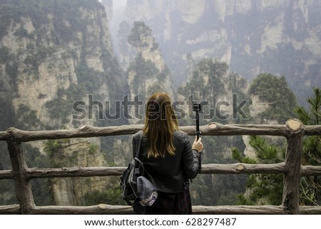 Young female tourist wear black leather jacket with gopro camera taking photo and enjoying mountain view, the Zhangjiajie National Forest Park, Hunan Province, China. 