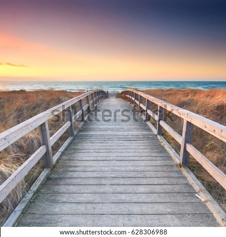 Wooden path at Baltic sea over sand dunes with ocean view, sunset summer evening                                 Royalty-Free Stock Photo #628306988