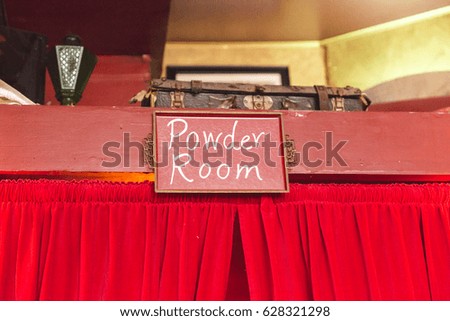 "Powder Room" words on sign over red curtains.