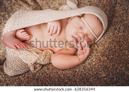 Sleeping newborn baby girl. Baby girl lies wrapped in a beige knit fabric.