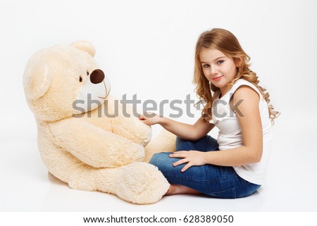 Girl sitting on floor with toy bear holding his paw.