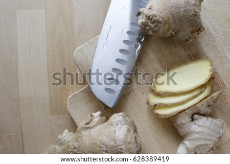 Pieces of ginger root on a wooden plate with a knife besides them.