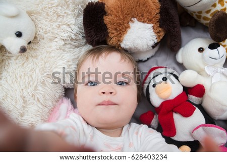 Funny baby girl taking photo of herself with favourite toys
