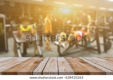 Empty brown wooden table top on blurred background of fitness gym,Young People group of women and men doing sport,interior of new modern club with equipment