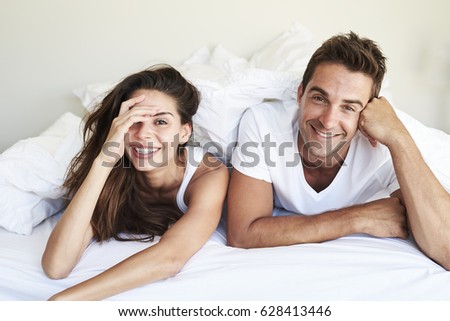 Happy couple lying and grinning in bed, portrait