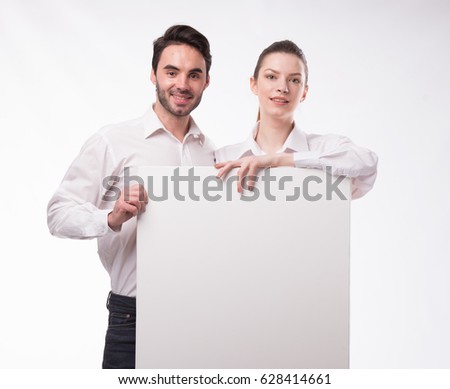 Young happy couple portrait of a confident businessman showing presentation, pointing paper placard gray background. Ideal for banners, registration forms, presentation, landings, presenting concept