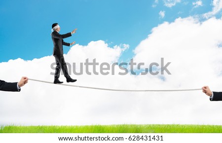 Businessman with blindfolder on eyes walking on rope over natural background