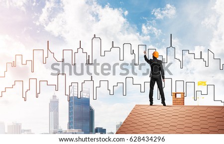 Engineer man standing with back on house roof and drawing city. Mixed media