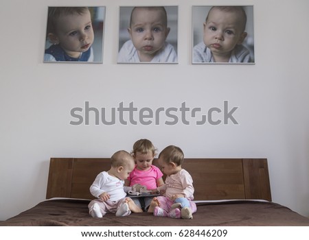 Three little sisters play on the bed and their portraits hang on the wall