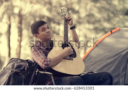 Smiling young man sitting near touristic tent and playing guitar
