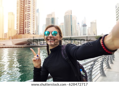 Young woman tourist laughing and taking selfie photo in Dubai Marina,Dubai,United Arab Emirates. Female traveler and photographer takes picture for her blog.Young happy tourist making selfie photo 