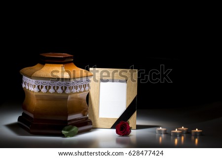 Wooden cemetery urn with blank mourning frame and flower on dark background