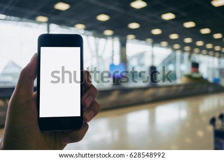 Mockup image of a man holding black mobile phone with blank white screen while standing and waiting for baggage claim in the airport
