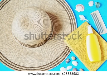 Summer rest at the sea. Female hat, yellow cosmetic bag, sunscreen, a wooden comb and seashells on a blue background. Flat lay composition. Beach holidays concept. Top view photography
