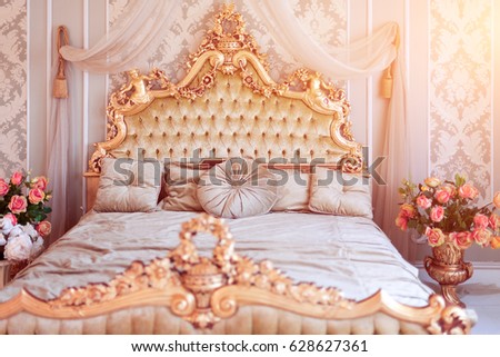 Luxury bedroom in light colors with golden furniture details. Big comfortable double royal bed in elegant classic interior. Toned picture
