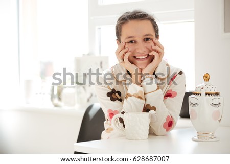 Smiling young woman wearing pajamas sitting in kitchen
