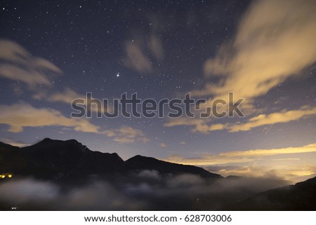 Night landscape with stars and illuminated village in the mountains