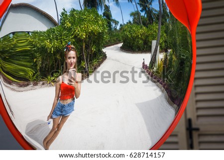 A beautiful woman taking selfie at small sand street in reflection of traffic mirror, showing beauty of the tropical island in Maldives