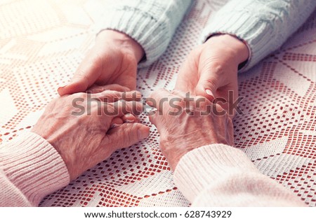 Care is at home of elderly. Senior woman with their caregiver at home. Concept of health care for elderly old people, disabled. Elderly woman holding hands closeup. Space for text white background.