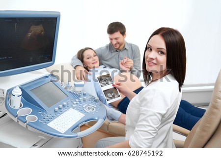 Attractive female gynecologist smiling happily to the camera while working with her pregnant patient copyspace pregnancy expecting family medical practitioner occupation modern technology sonogram.