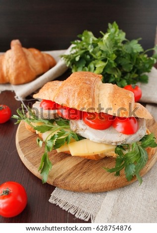 Croissant sandwich with bacon, cheese, lettuce and tomato on white wooden table. Healthy snack.