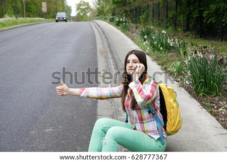  young girl tourists hitchhiking along a road