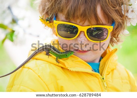 Boy and lizard, green lizard sits on a child in a yellow jacket, cute beautiful
boy with freckles and his friend lacerta emerald on a spring background of greenery