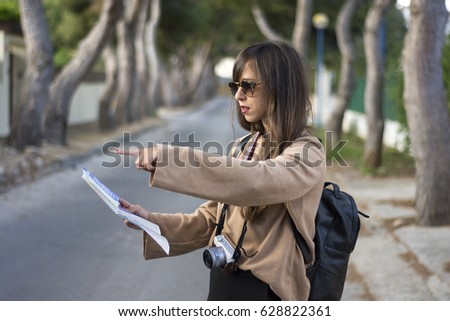 Beautiful stylish girl is studying the map, pointing away and smiling while traveling
