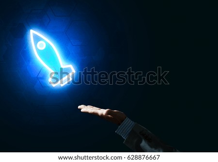 Rocket glowing icon and businessman hand on dark background