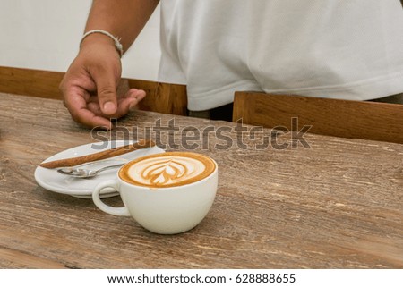 Man is setting hot capucchino in the white cup on the brown wooden table for making photo stock for sale.