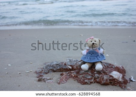 Teddy bear sits alone on the stone at the beach looking out to sea.