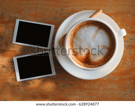 Coffee latte art and blank picture frame on vintage wood table in morning light