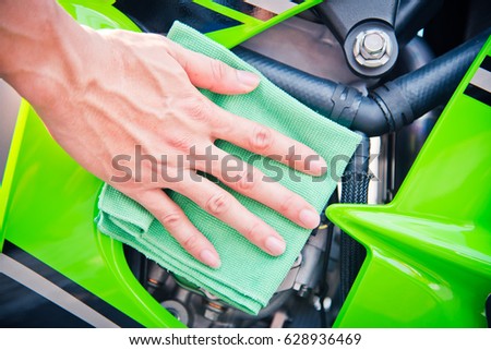 Hand with man cleaning motorcycle with green microfiber cloth
