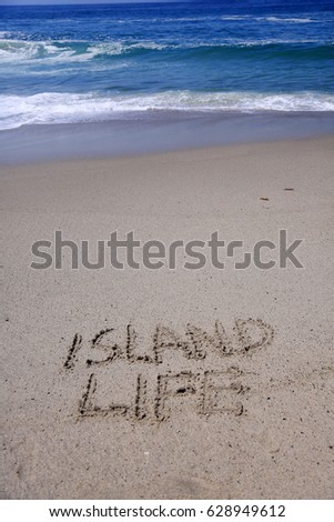 words Island Life written in sand on the beach with the ocean tide and waves