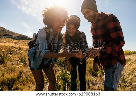 Group of hikers looking at pictures on mobile phone and laughing. Happy young people hiking in countryside.