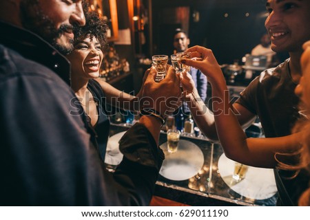 Friends toasting each other with shots of vodka as they enjoy a relaxing night out together at the pub. Group of friends together having fun Royalty-Free Stock Photo #629011190
