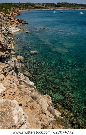 Beautiful turquoise see and cliffs on a sunny clear day with some boats in the background. Captured in Seu Coast, Oristano province, Sardinia, Italy.