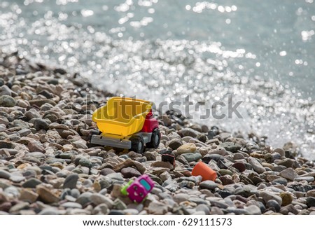 Bright plastic little baby toy cars on a pebble beach near the sea. Waiting for summer.