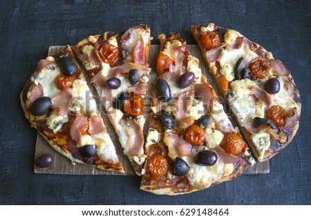 Cut into slices of delicious fresh pizza with ham on a dark background. The view from the top . Pizza on the black table.
