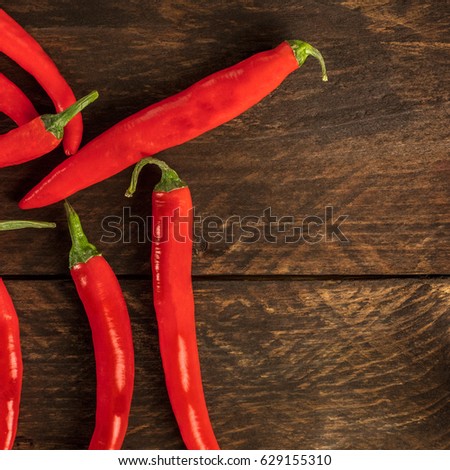 A square photo of red hot chili peppers, shot from above on a dark brown wooden texture, with copyspace