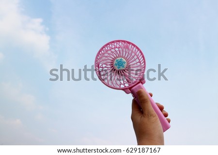 Mini pink portable fan with hand holding handle mini fan shows in light blue clouds sky  background