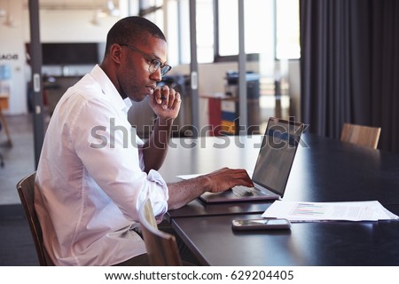 Young black man in wearing glasses using laptop in office