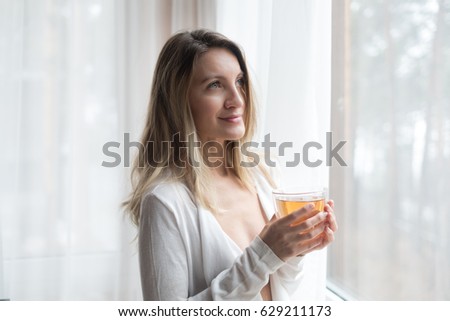 the beautiful woman with a cup of tea looks out of the window