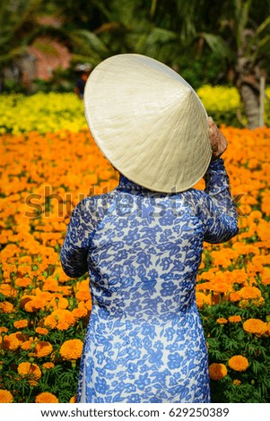 Vietnamese woman in traditional dress with a conical hat, standing on flower field