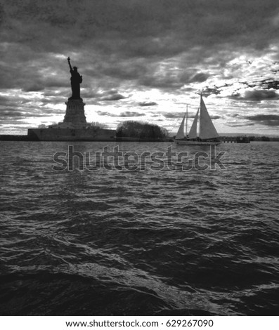 Liberty Island at dusk in black and white with sailboat.