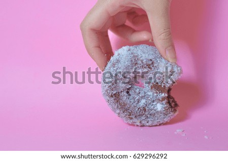 Image of chocolate donut coated with shredded coconut in a sweet pink background The donut was held by a hand. This image is showing that eating is happiness.