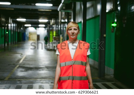 female employee in an orange robe vest in the working space of a production facility, exercises control in warehouse production areas