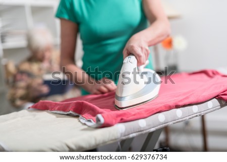 Home helper ironing clothes for elderly woman Royalty-Free Stock Photo #629376734